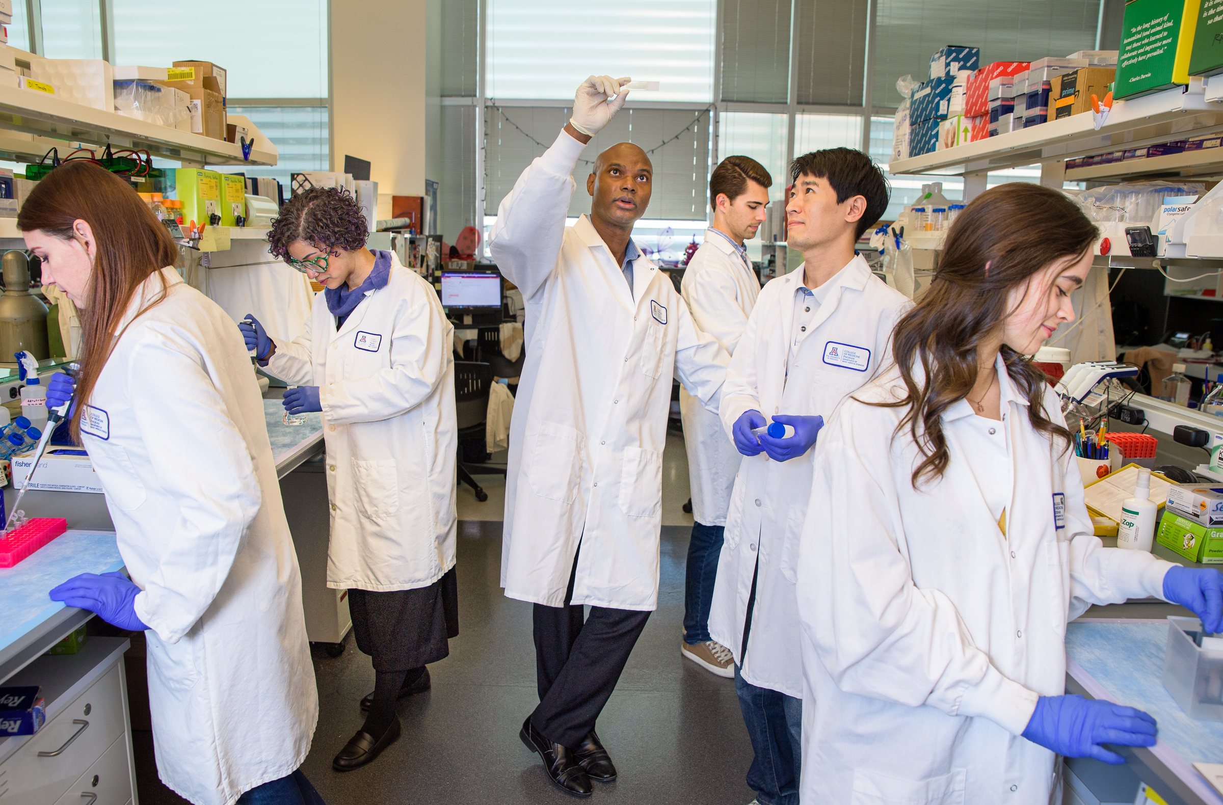 Deveroux Ferguson holds a sample up to the light while lab members work at the benches around him